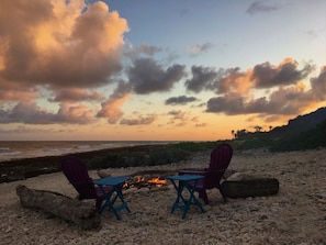 A beach scene with two chairs and a small table around a campfire, overlooking the ocean and a rocky shoreline. - Magical oceanfront home with pool - 2 bedroom, 2.5 baths, sleeps 6-8, built 2017 (Cayman Brac, Sister Islands)