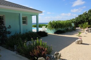 A turquoise building with a pool and a garden with tropical plants. - Magical oceanfront home with pool - 2 bedroom, 2.5 baths, sleeps 6-8, built 2017 (Cayman Brac, Sister Islands)