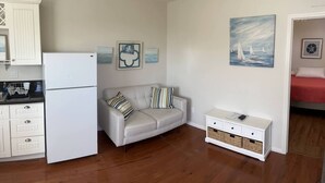 A compact living space with a kitchenette, a sofa, a side table, and artwork on the walls.