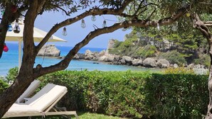 A lounge chair under a tree with hanging light bulbs, overlooking a coastal area with rocky cliffs and a clear blue sea. - Corfu Dream Holidays Apartment (Corfu island)