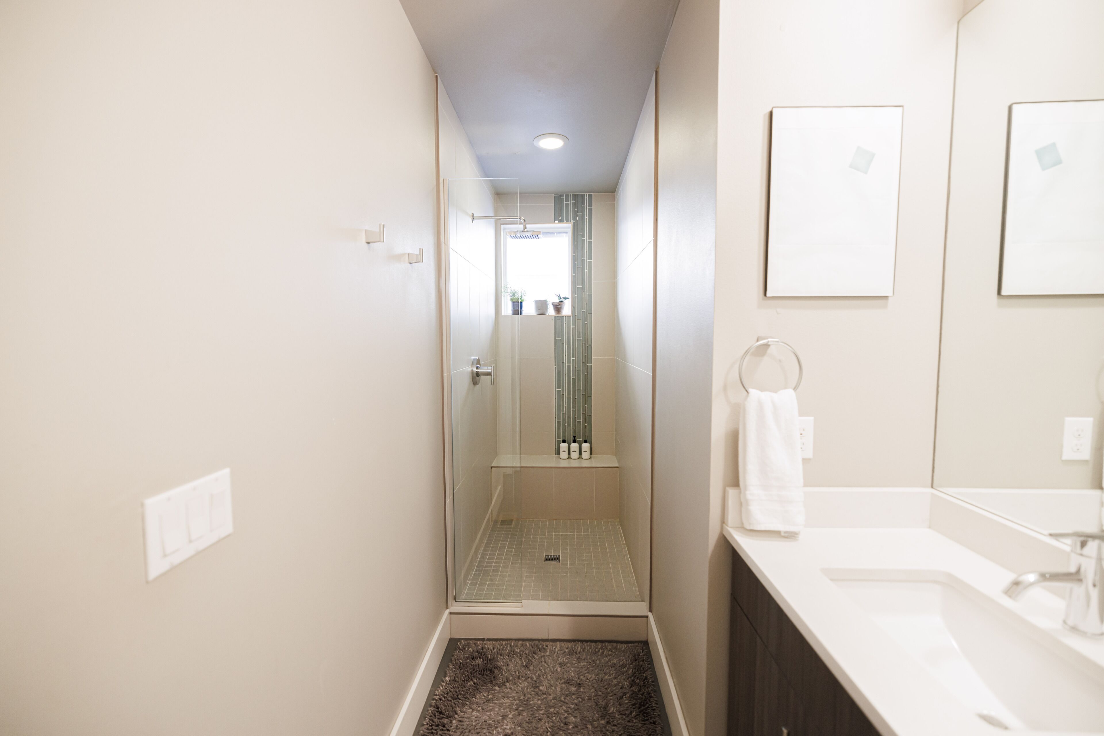 A narrow bathroom with a shower, a sink, and a mirror.