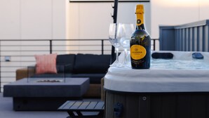 Una vasca idromassaggio con una bottiglia di champagne Lacticosa e due bicchieri su un terrazzo panoramico.