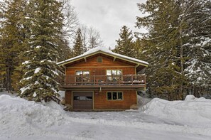 A two-story log cabin with a balcony, surrounded by snow-covered trees.
