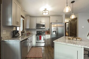 A modern kitchen with stainless steel appliances, white cabinetry, granite countertops, and pendant lighting.