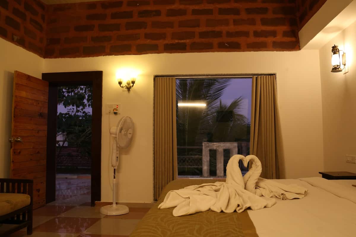 Ein Hotelzimmer mit einem Bett, einem Ventilator, einem Fenster mit Vorhängen, einer Holztür und einer wandmontierten Leuchte.
