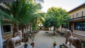 A courtyard with two lion statues, palm trees, and a building with a tiled roof.