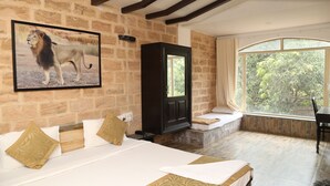 A bedroom with a large bed, a television, a window with a view of trees, and a stone wall.