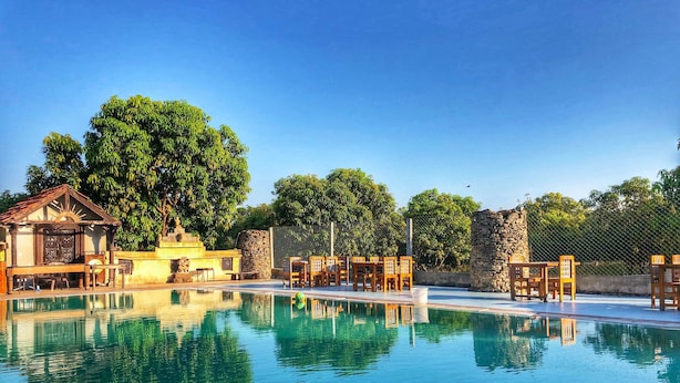 A clear swimming pool with wooden lounge chairs and a small pavilion.