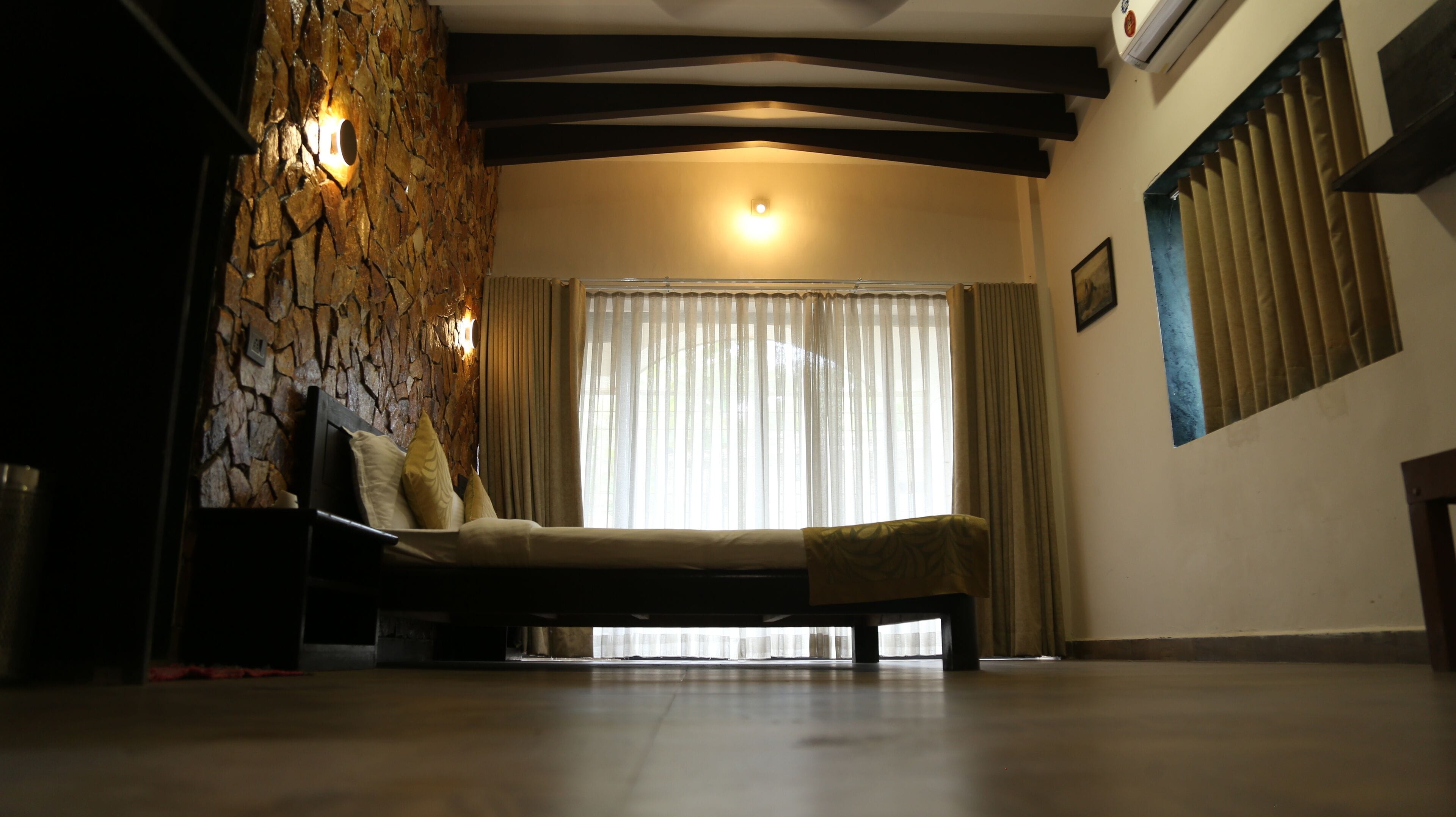 Una habitación con pared de piedra, una cama, un ventanal con cortinas y un radiador.