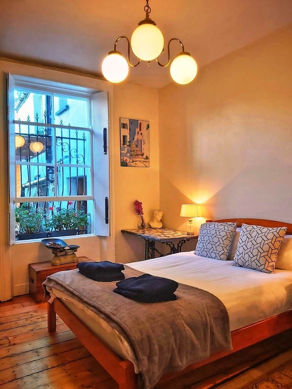 A bedroom with a bed, bedside table, lamp, and a painting on the wall.