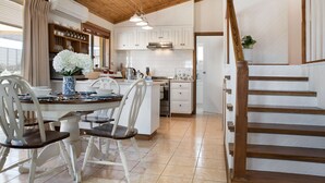 Una cocina con armarios blancos, techo de madera y un comedor con sillas y mesa blancos.