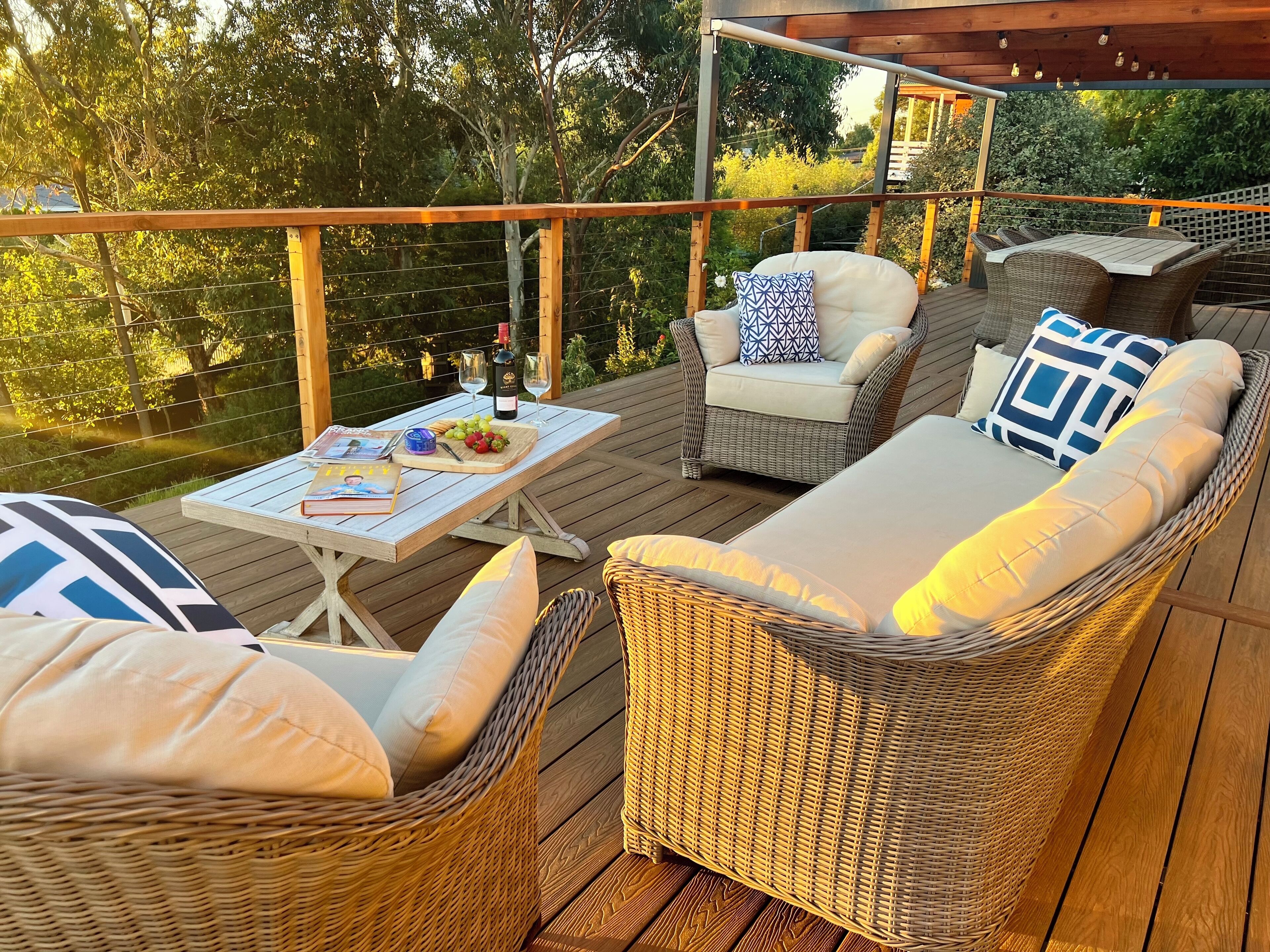 A wooden deck with wicker furniture, including a sofa and chairs, and a table with a bottle and glasses.