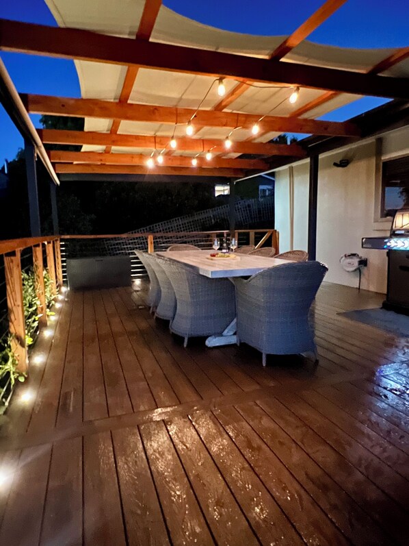 An outdoor deck with a wooden table and chairs, string lights, and a grill. - A cozy, inviting country retreat with a little modern flair. (Daylesford)