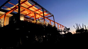 Una casa moderna de vidrio con estructura metálica, rodeada de vegetación.