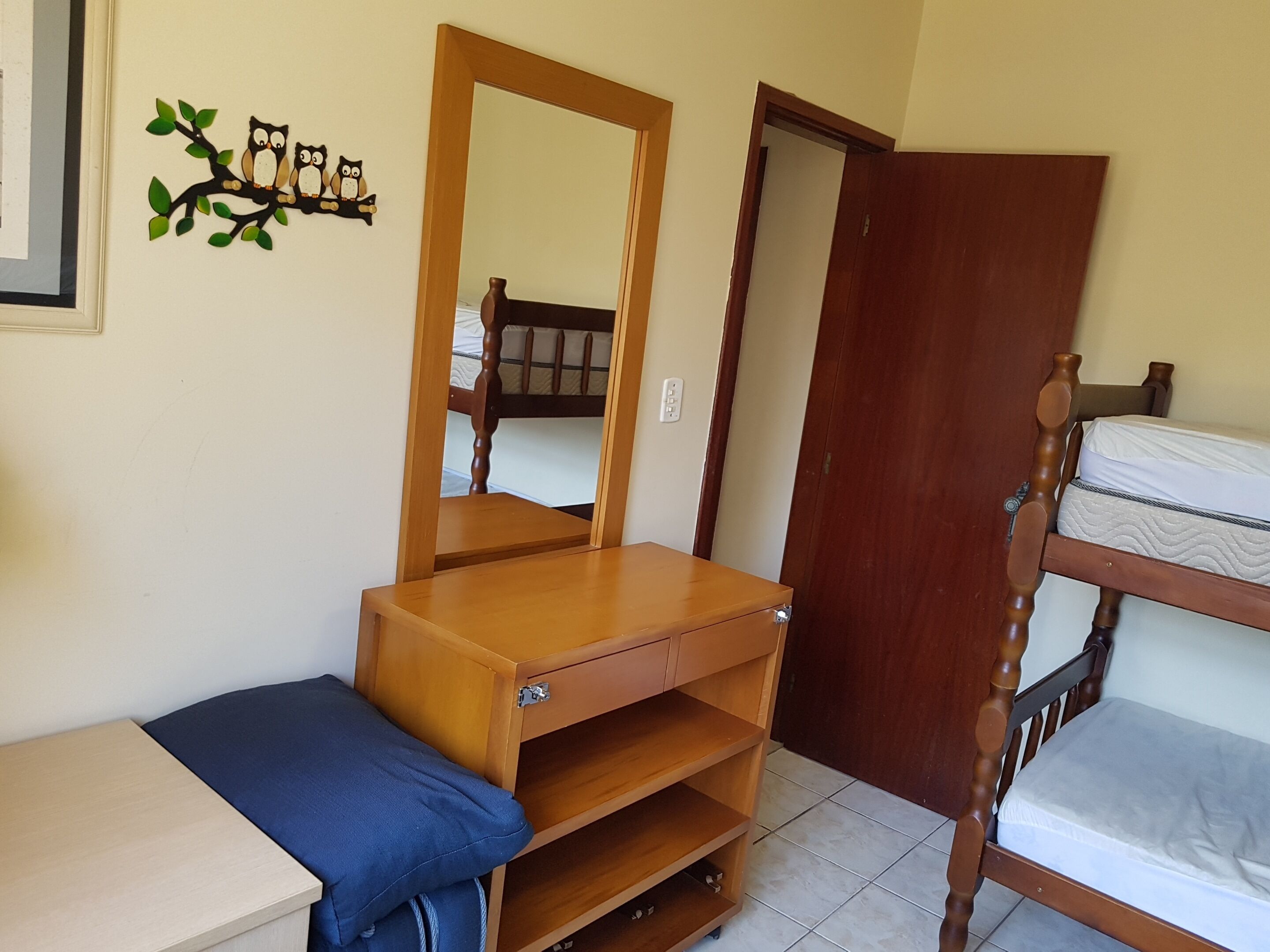 Un dormitorio con cómoda de madera, espejo, literas y estante de pared con búhos decorativos.