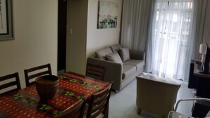 En stue med sofa, spisebord med stole, ventilator i loftet og et vindue med gardiner.