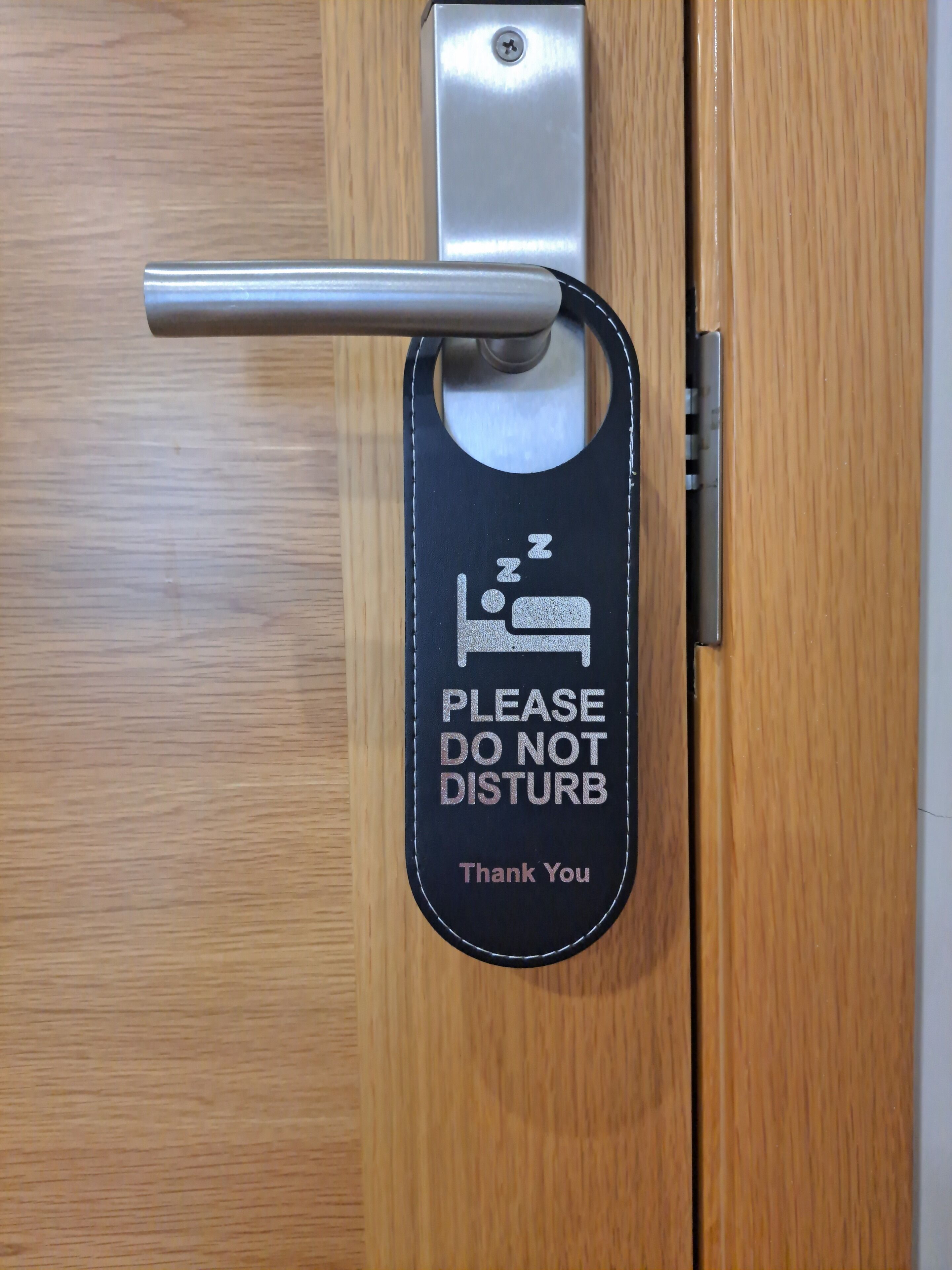 A door with a black sign that reads "PLEASE DO NOT DISTURB Thank You" and a bed symbol.