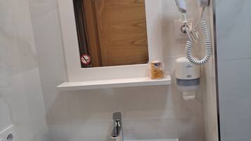 A bathroom with a white sink, a mirror, a hairdryer, and a shelf with a bottle.