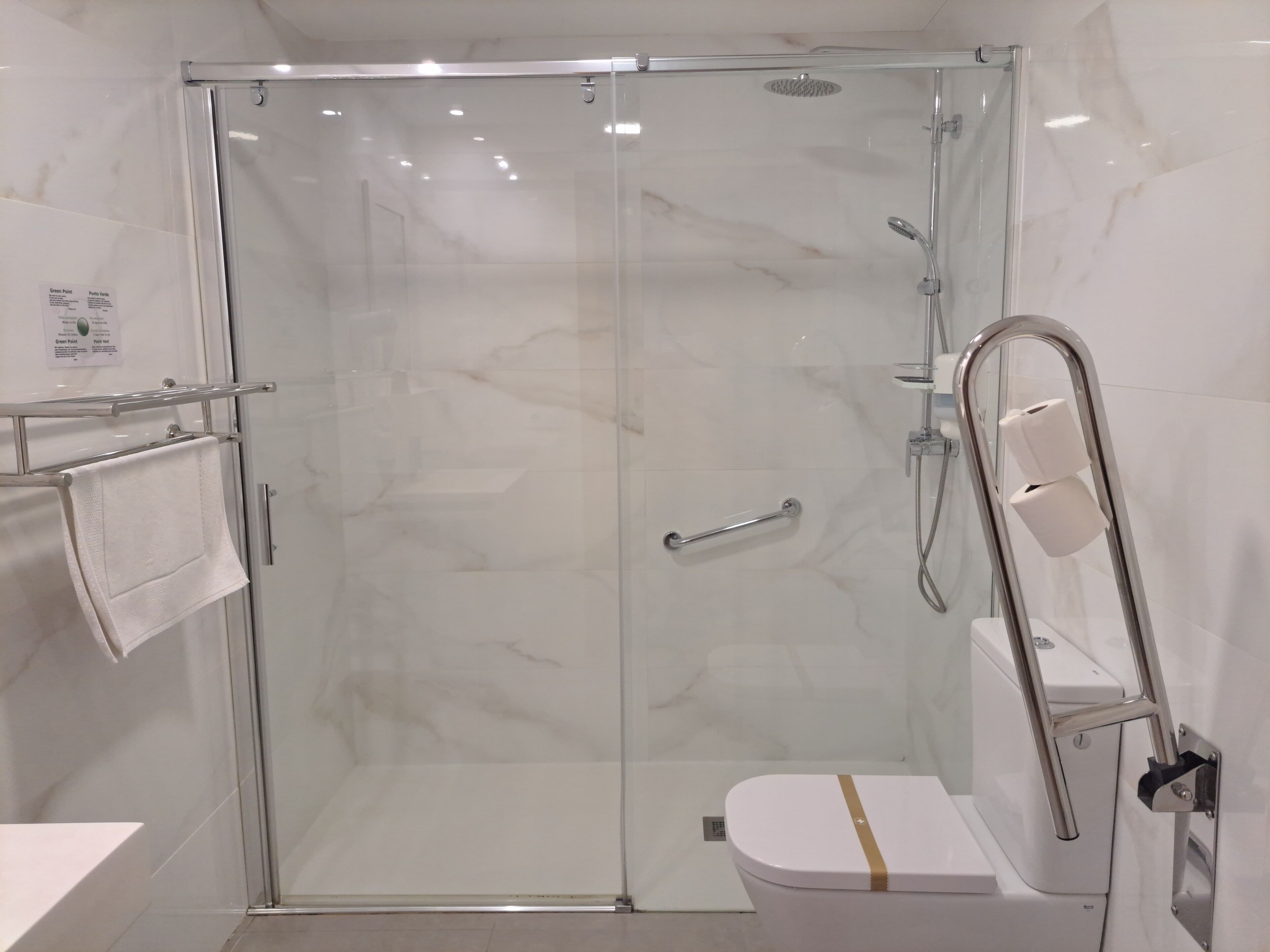 A modern bathroom with a glass-enclosed shower, a white toilet, and a handrail.