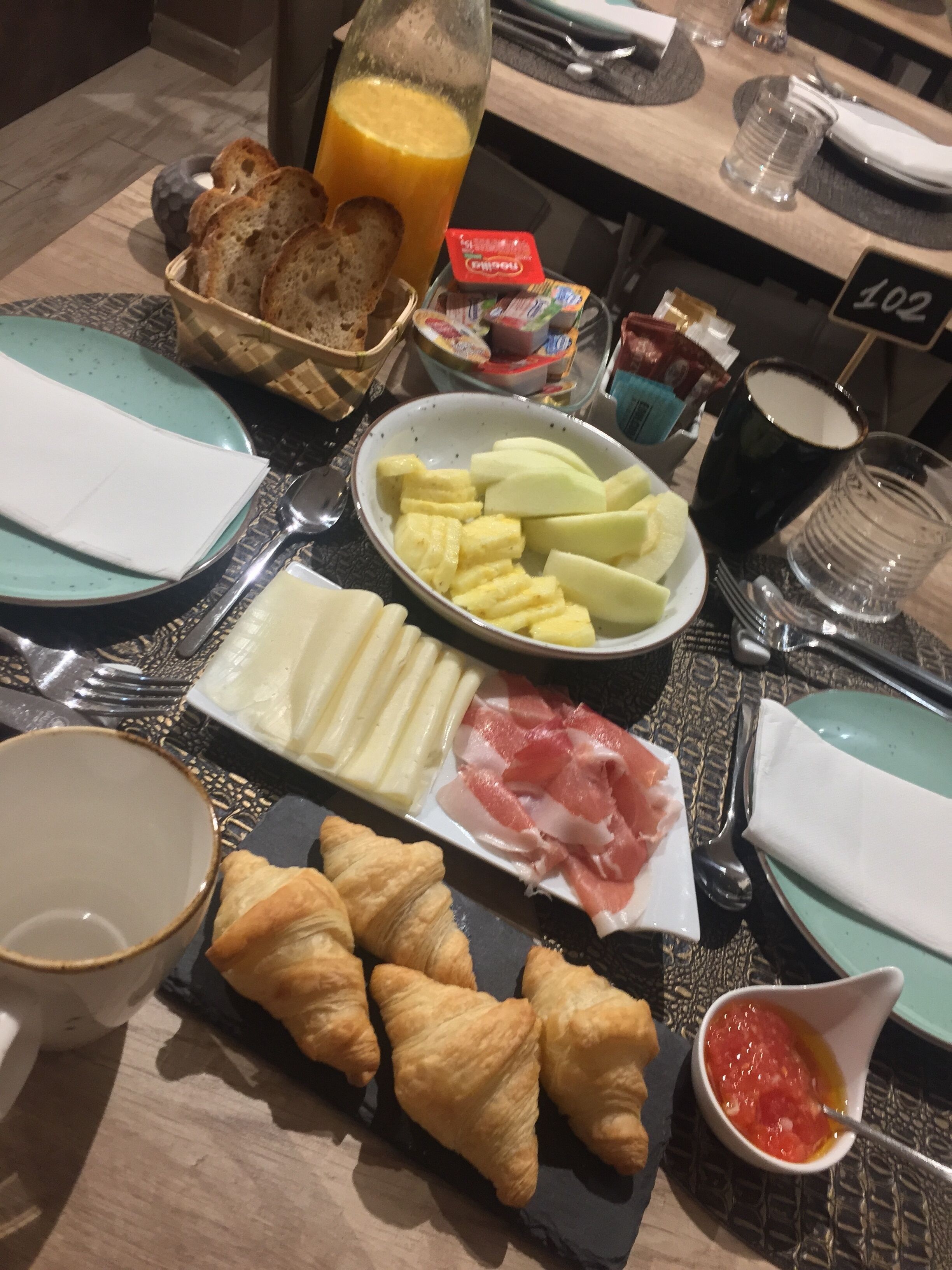 Una mesa de desayuno con croissants, queso, jamón y fruta.