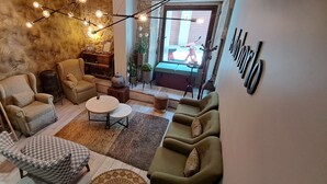 Een gezellige woonkamer met een bank, fauteuils, een salontafel en een stoel. Er staat een kapstok en een tafeltje met decoratieve objecten.