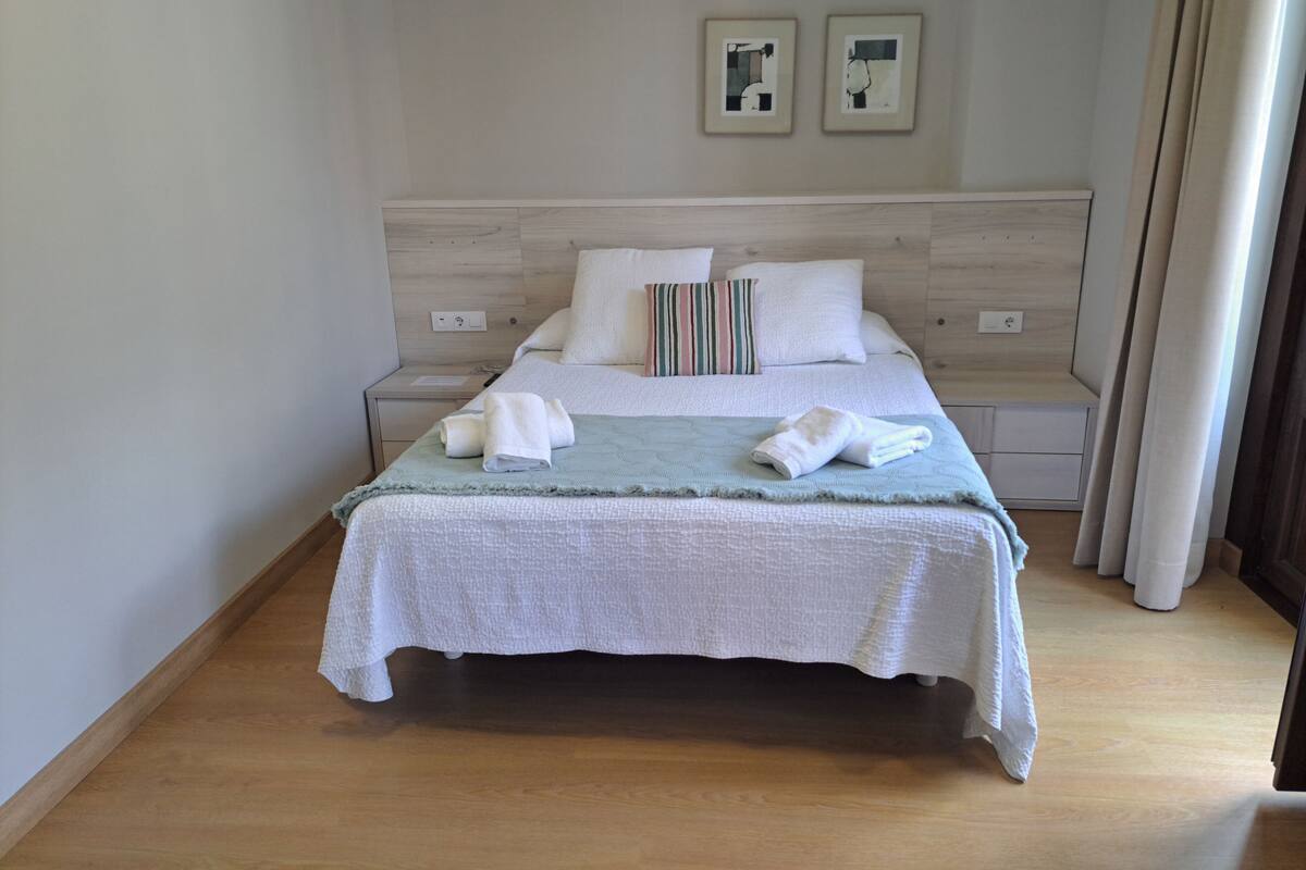 Una cama bien hecha con sábanas blancas y una manta azul claro, un cabecero de madera y dos cuadros en la pared.
