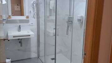 A modern bathroom with a glass-enclosed shower, a white sink, and a mirror above the sink.
