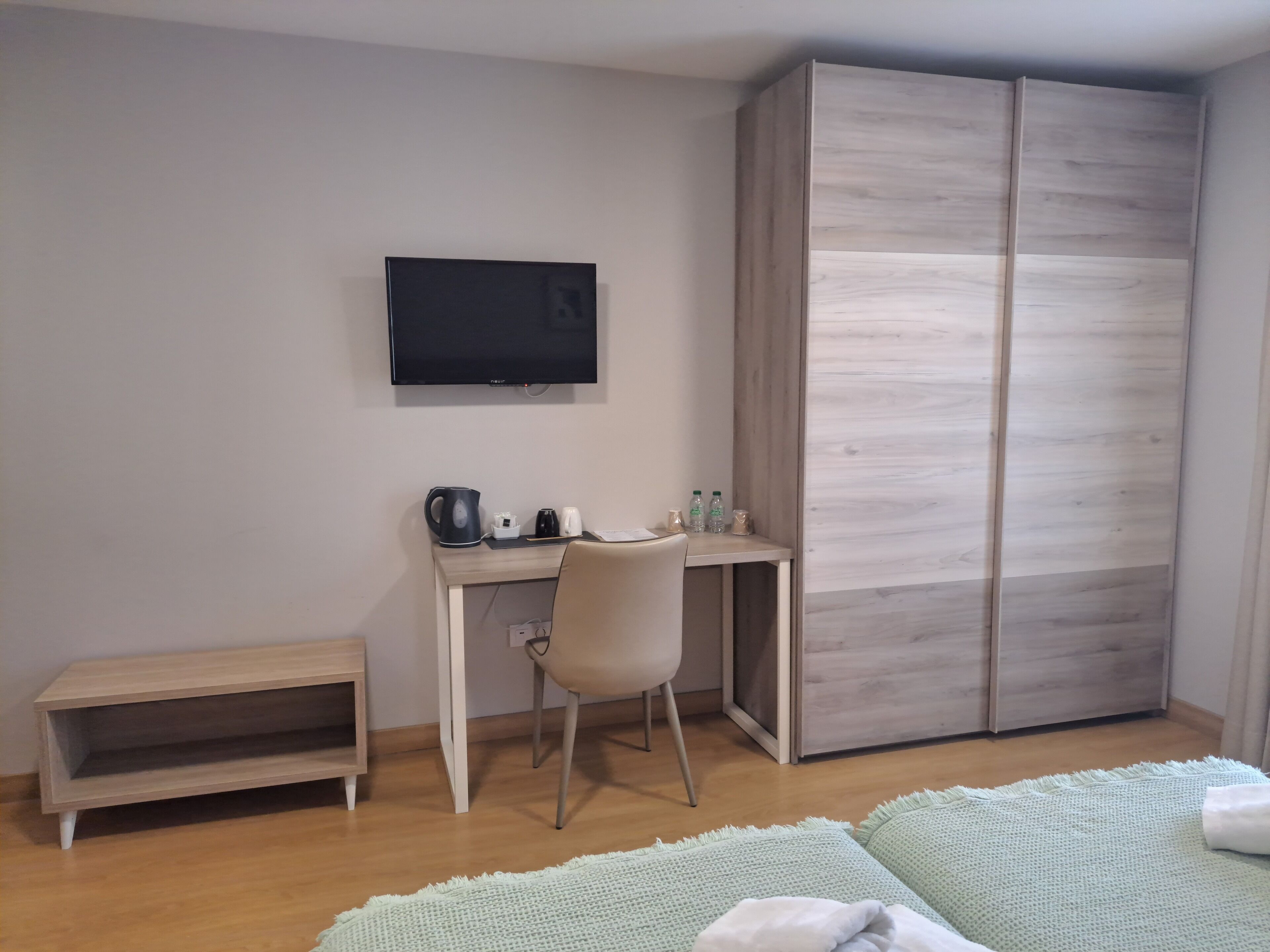 A bedroom with a bed, a desk with a chair, a television, and a wardrobe.