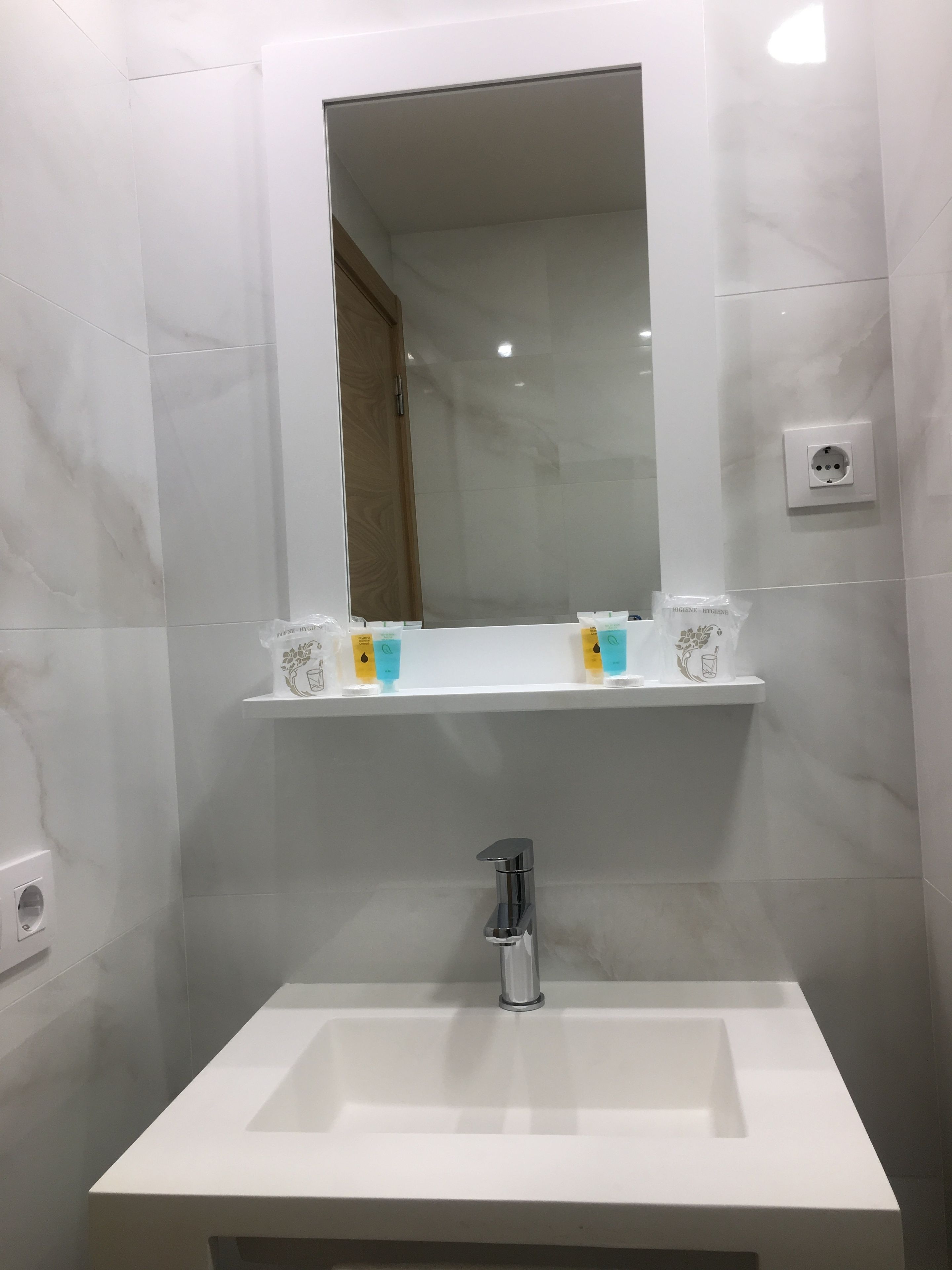 Un baño con lavamanos blanco, un espejo y dos repisas con artículos de aseo.