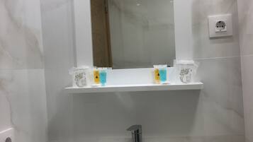 Un baño con lavamanos blanco, un espejo y dos repisas con artículos de aseo.