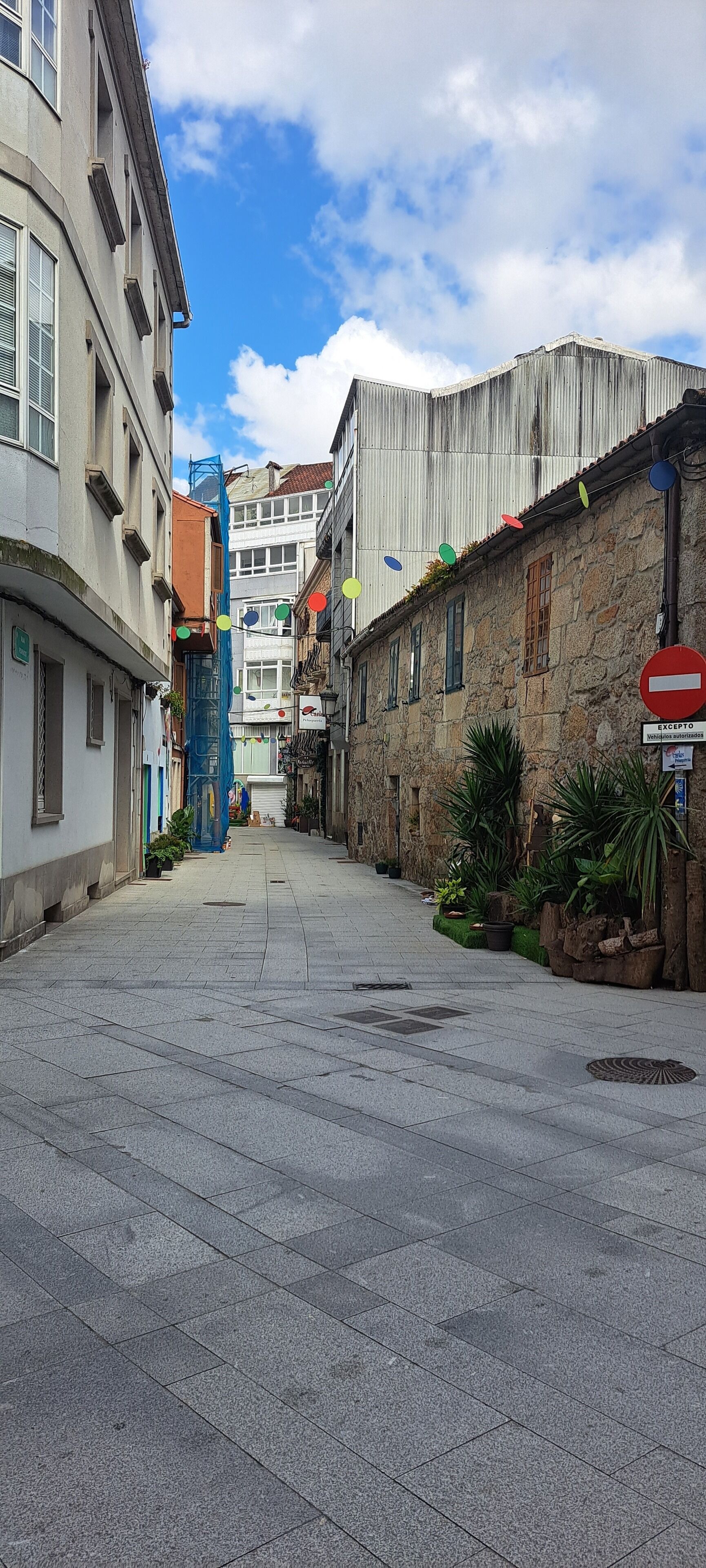 A narrow street with stone buildings, a blue construction crane, and a no-entry sign.