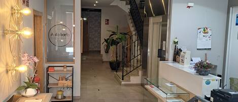 Zona de recepción de hotel con un escritorio, una escalera y un cartel que indica "Zona de Secado".