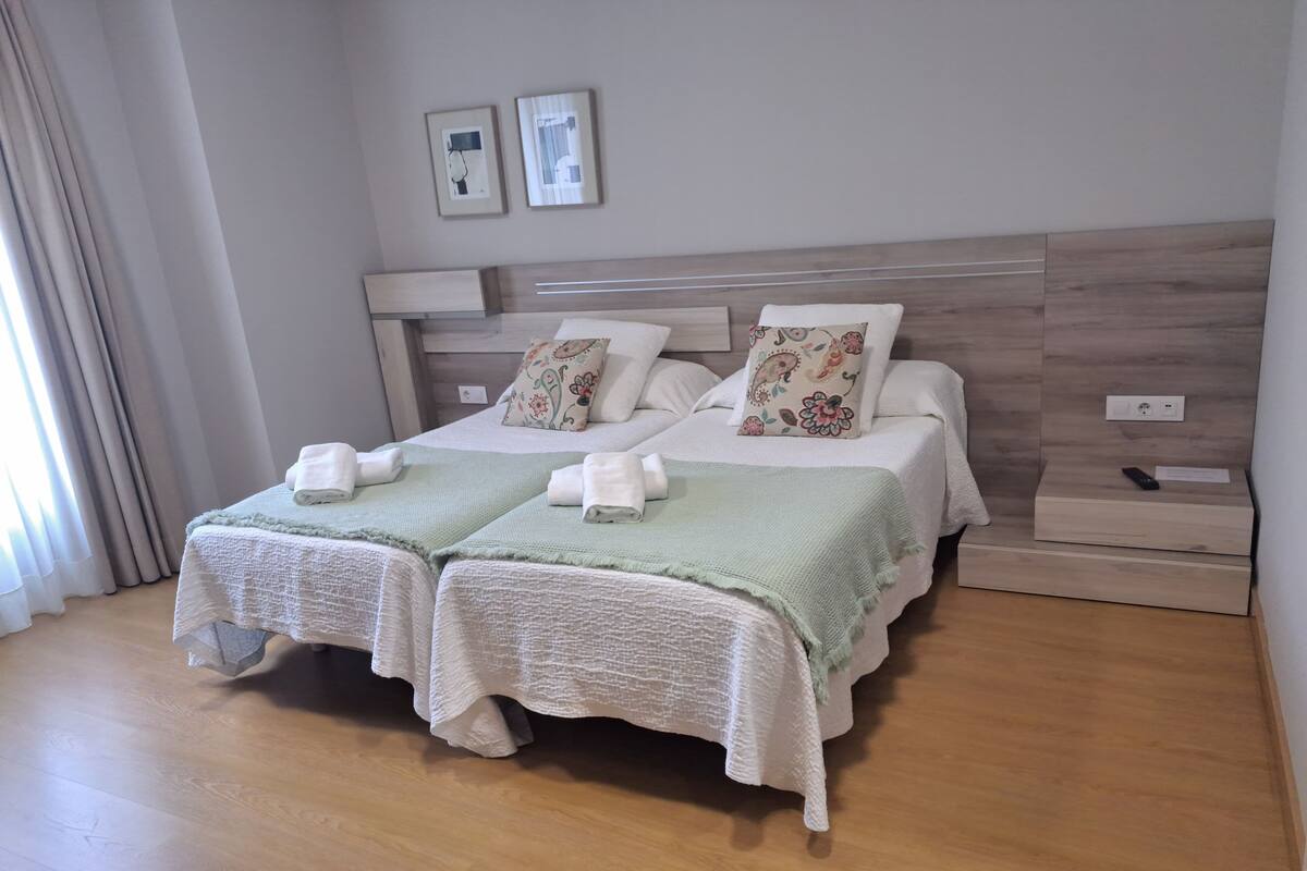 Una cama doble con dos almohadas, una mesita de noche y una lámpara en la pared.