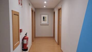A hallway with wooden flooring, a fire extinguisher mounted on the wall, and a framed picture on the wall.