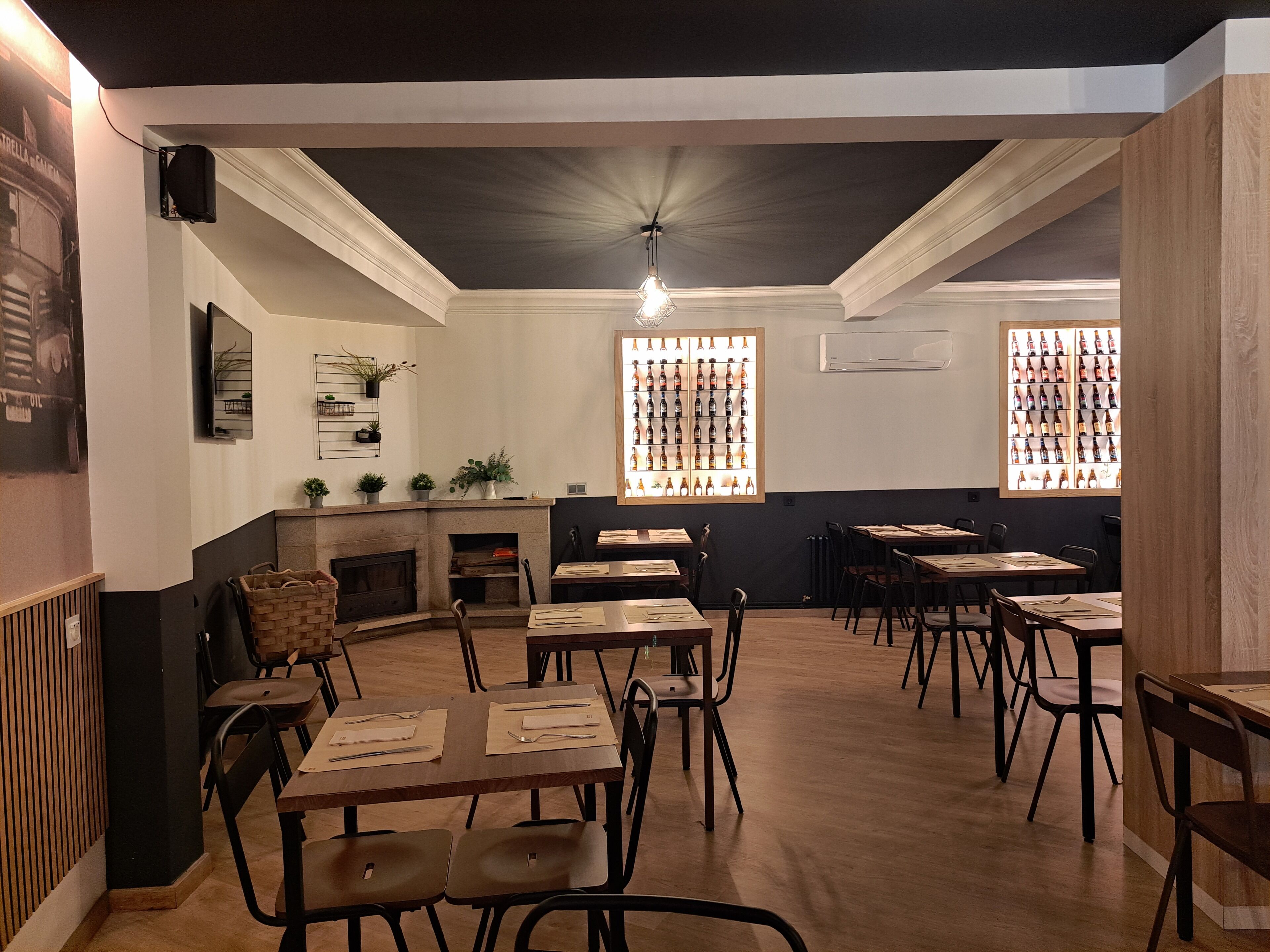 A restaurant interior with multiple tables and chairs, a fireplace, and a wall displaying bottles.