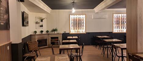 A restaurant interior with multiple tables and chairs, a fireplace, and a wall displaying bottles.