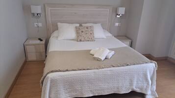 A neatly made bed with a white headboard, a floral pillow, and a folded towel on a textured blanket. There are two bedside tables with lamps and a nightstand with a remote control.