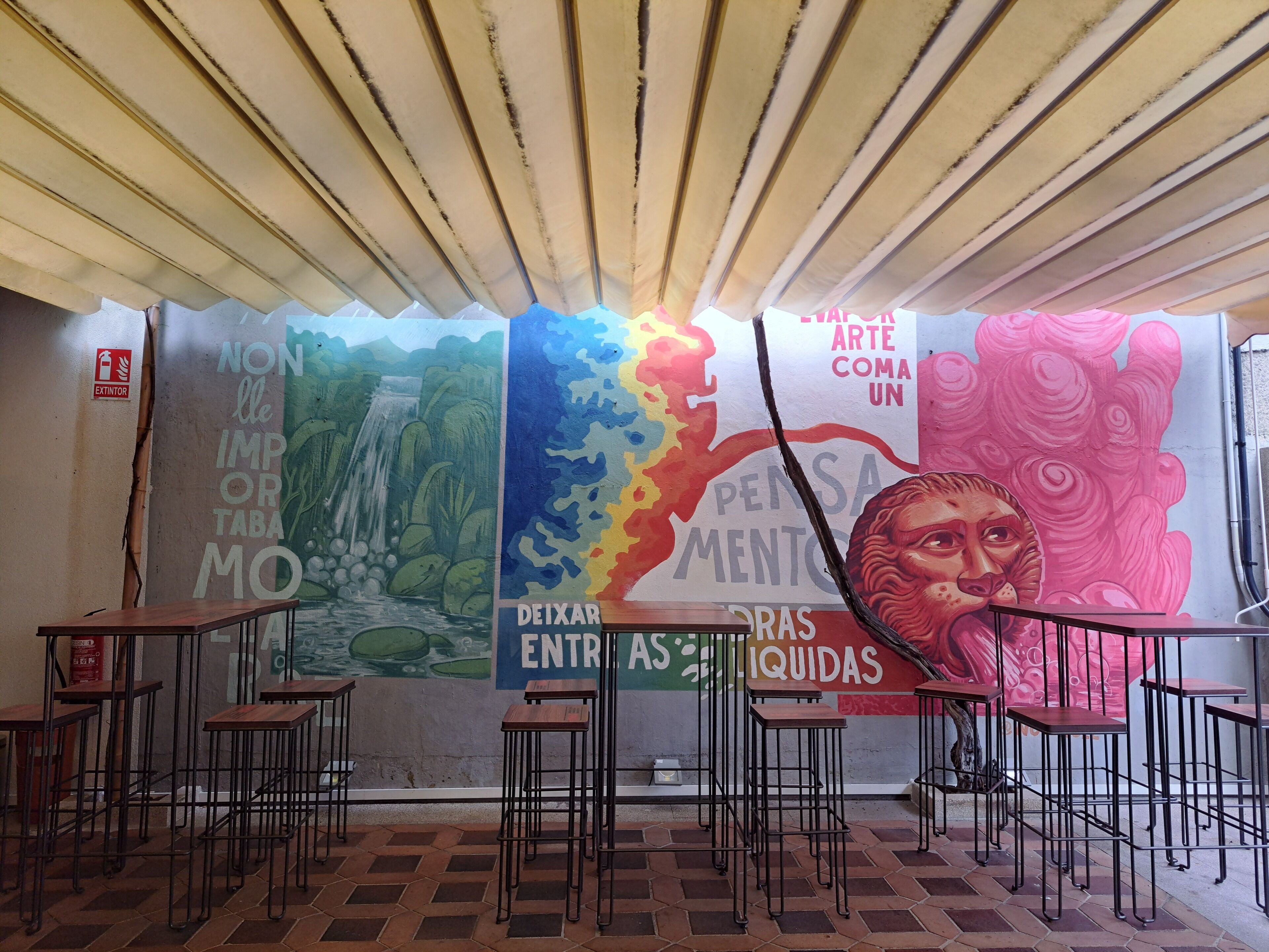 Interior de un restaurante con piso de baldosas, taburetes de metal y un mural con texto y coloridas ilustraciones.