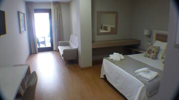 Habitación de hotel con cama, escritorio, silla, mesita, espejo y ventana con cortinas.