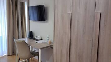 A room with a wooden wardrobe, a desk with a chair, a flat-screen TV, and a window with curtains.