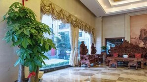 A lobby with a large potted plant, a checkered floor, a traditional wooden sofa, and a large painting on the wall. - King Lycra Hotel(Shenzhen International Convention and Exhibition Center store) (Shenzhen)