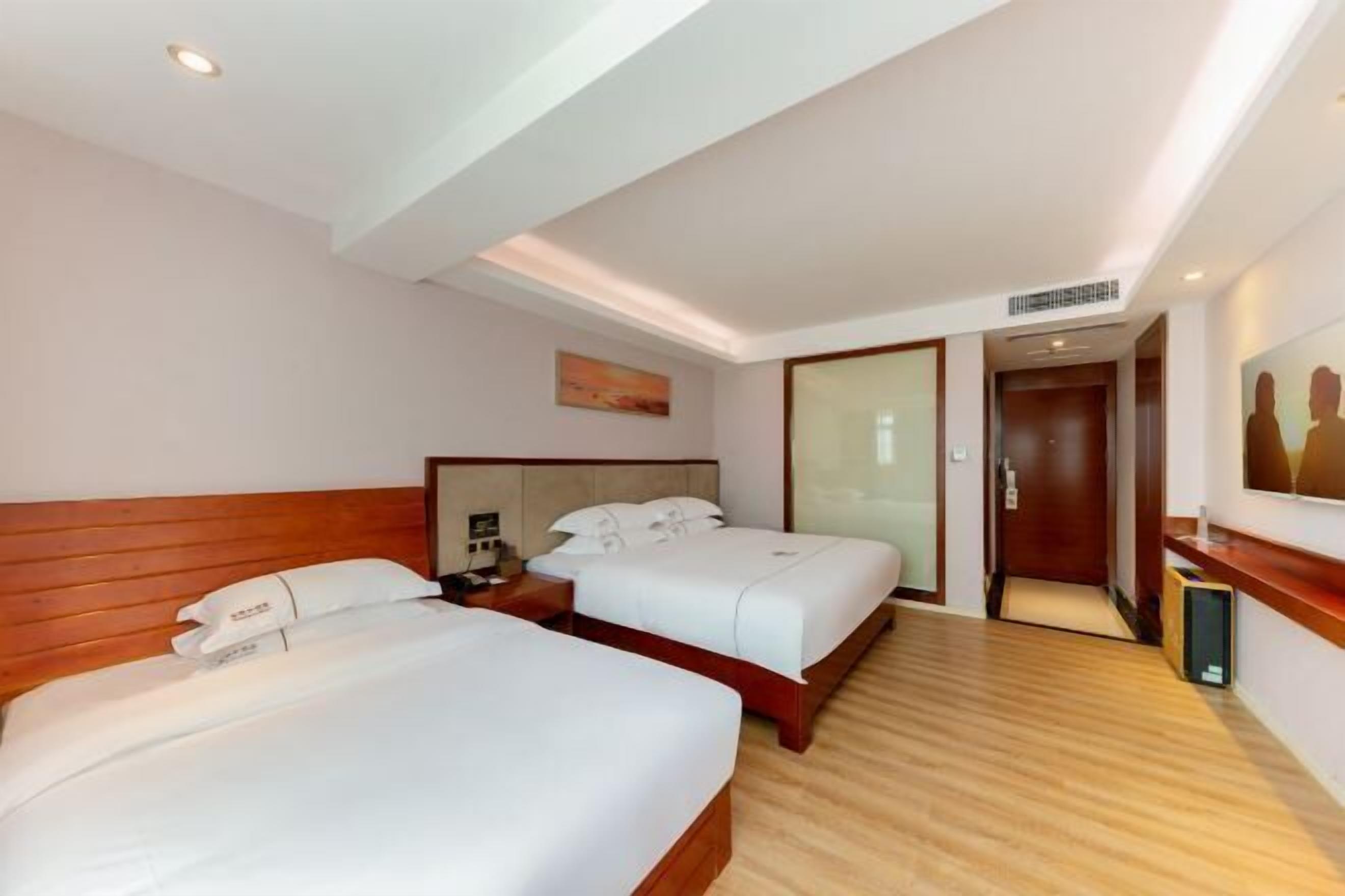 A hotel room with two beds, wooden headboards, a large mirror, and a painting on the wall.