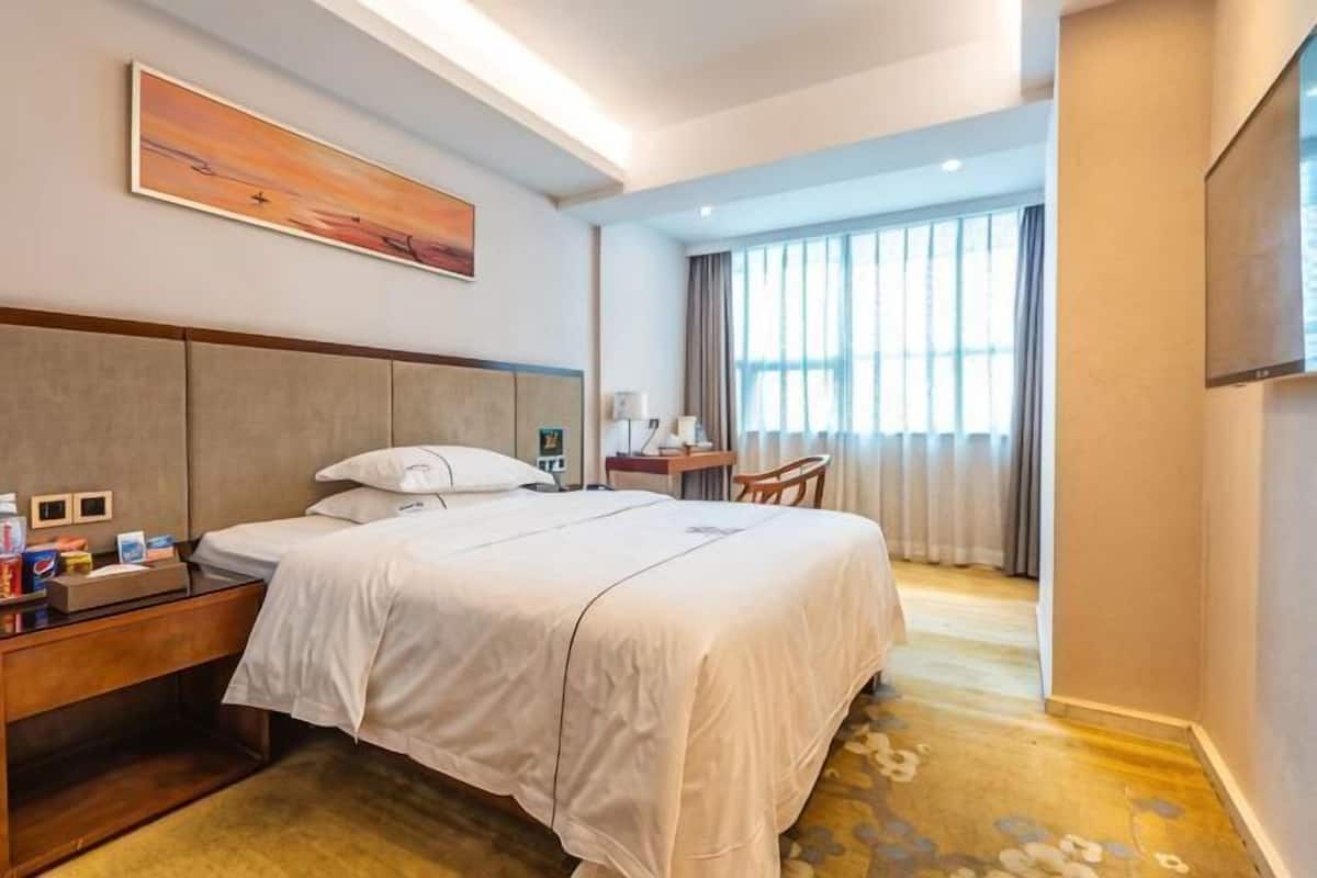 Habitación de hotel con una cama grande, mesita de noche, lámpara y vista al exterior por la ventana.