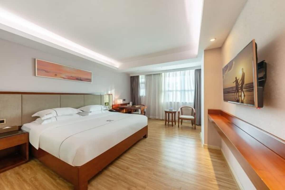 Habitación de hotel con una cama grande, mesitas de noche, un escritorio, una silla y un cuadro en la pared.