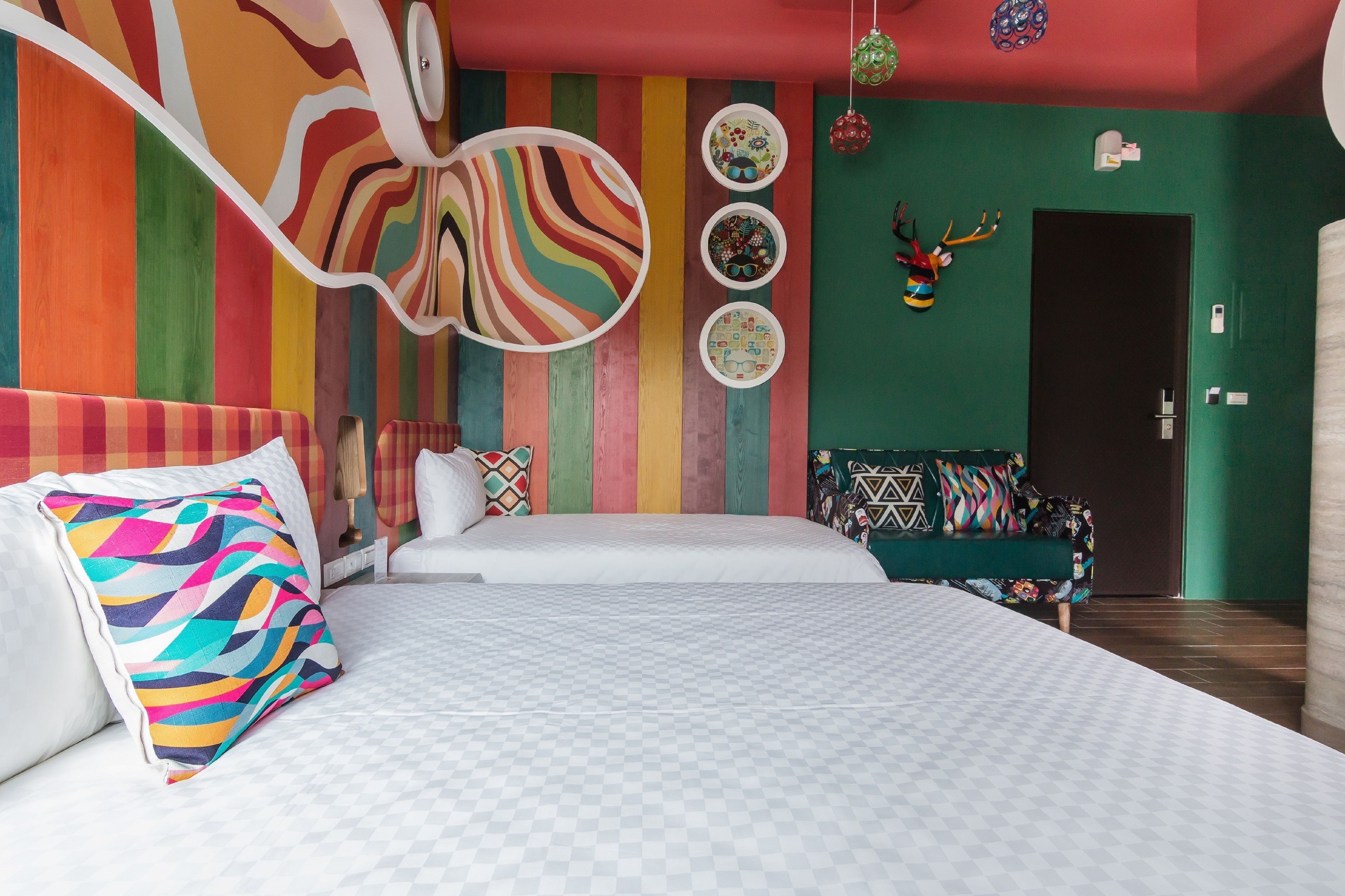 A modern hotel room with a large bed, a sofa, colorful wall art, and a decorative antler head.
