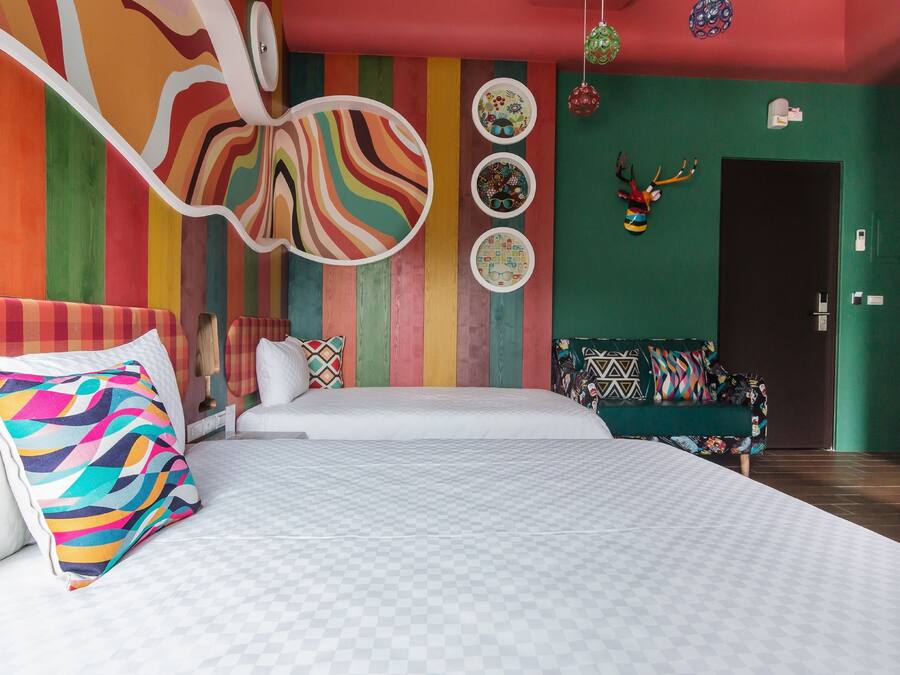 A modern hotel room with a large bed, a sofa, colorful wall art, and a decorative antler head.