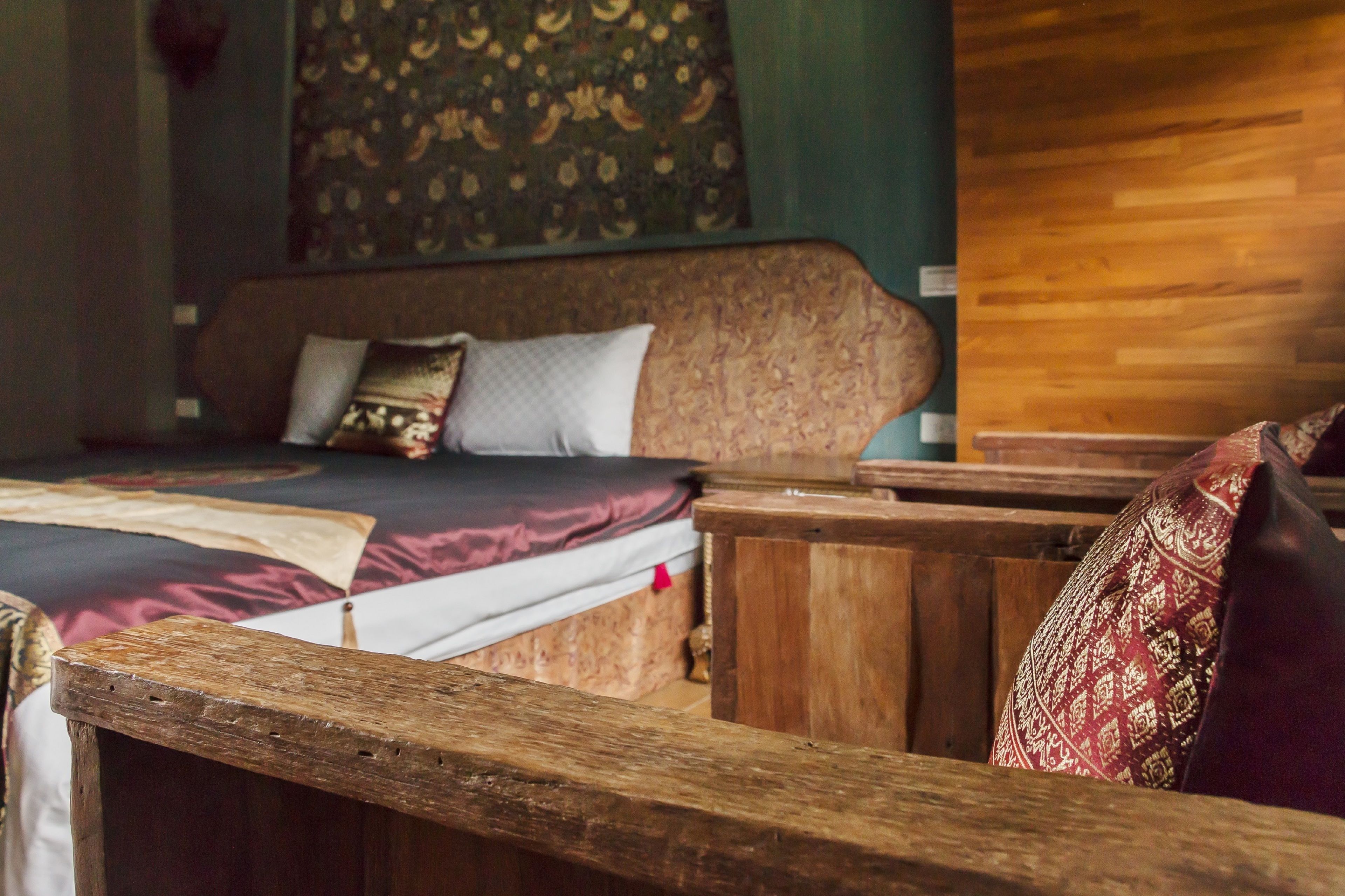 A wooden bed with a patterned headboard, a wooden bench, and a patterned cushion.