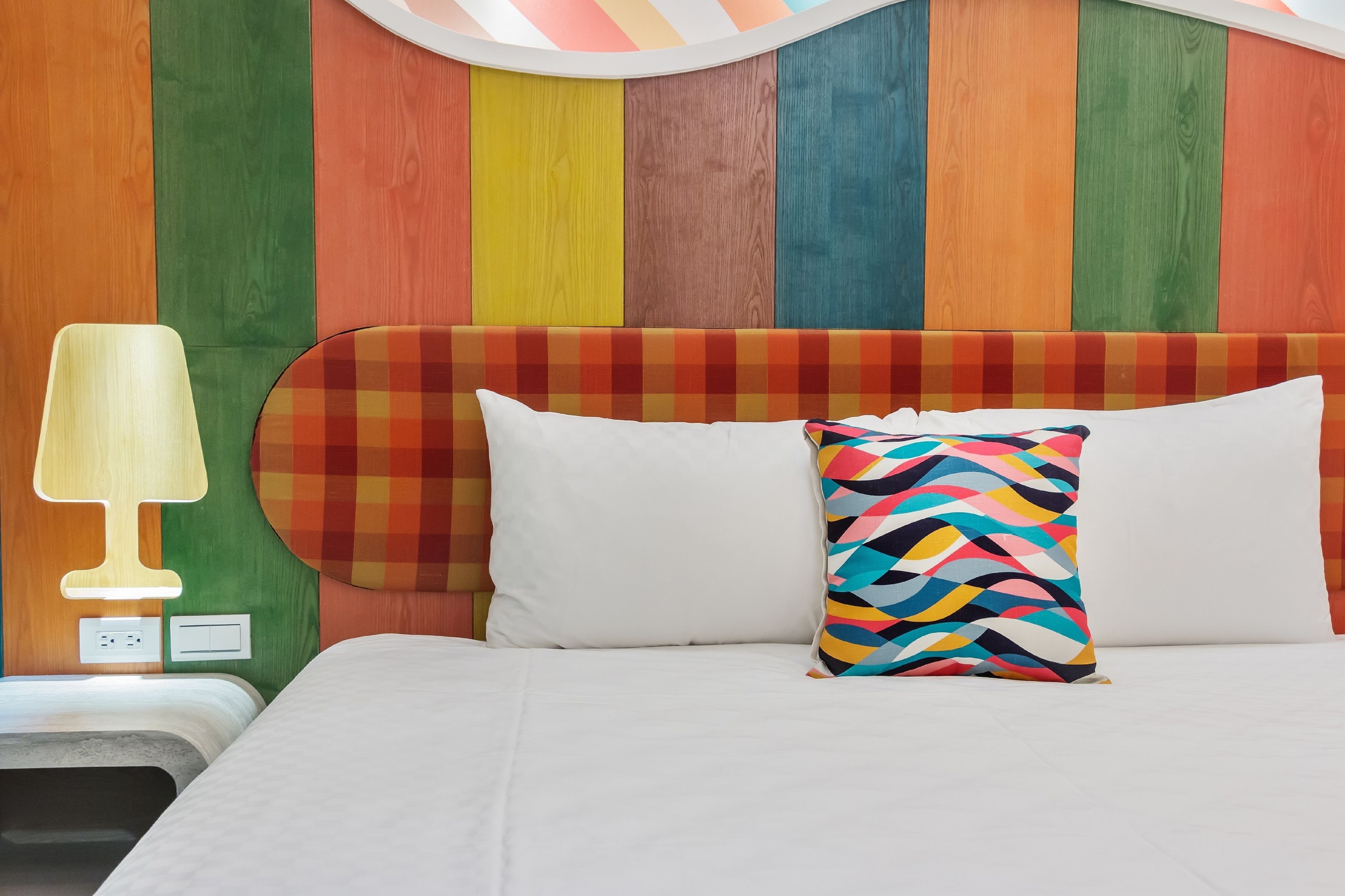 Una cama con un cabecero colorido, una lámpara de noche y un cojín estampado.