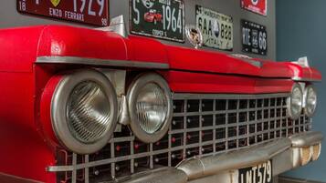 Un coche antiguo con una prominente parrilla frontal y faros, y varias placas de matrícula visibles en la pared de fondo.