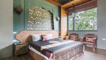 Un dormitorio con una cama grande, un cabecero decorativo, una mesita de noche, un banco y vistas a árboles a través de una ventana.